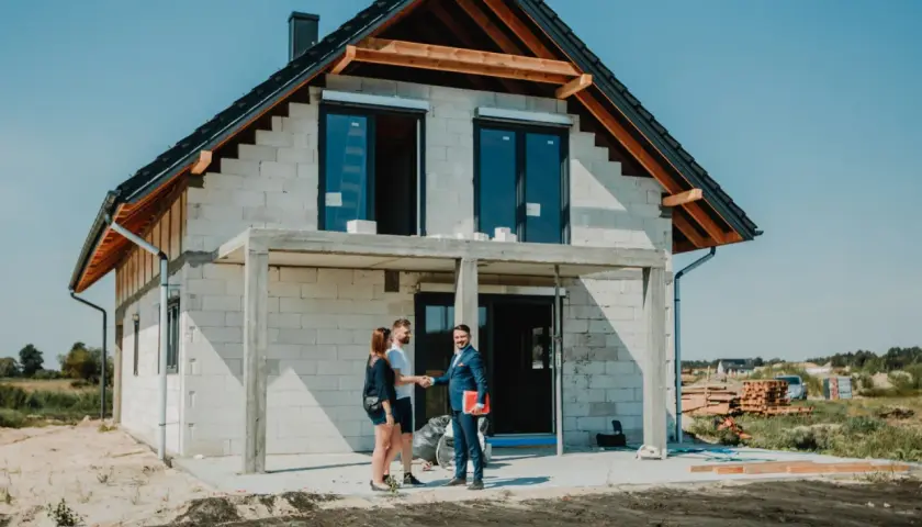 Para młoda wita się z doradcą finansowym przed budowanym domem. Marzenie o własnym gniazdku staje się realne dzięki kredytowi na budowę domu.