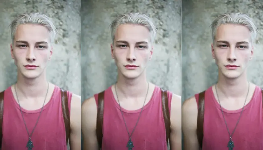 Joven con pelo blanco, viste camiseta rosa y un collar con un amuleto.