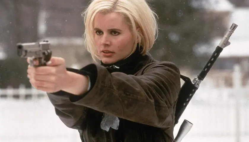 Geena Davis w filmach akcji, z pistoletem w dłoni i karabinem na ramieniu, gotowa do akcji w zimowej scenerii.