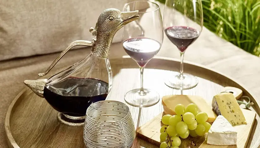 Dekantiert bedeutet, Wein in eine Karaffe zu füllen, um ihn zu belüften. Hier: ein Entenkaraffe mit Rotwein, Gläser, Käse und Trauben.