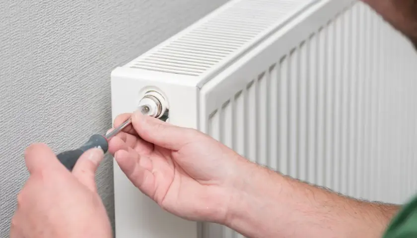 Mężczyzna używa śrubokręta do regulacji zaworu grzejnika aluminiowego. Dowiedz się, jak rozkręcić grzejnik aluminiowy.