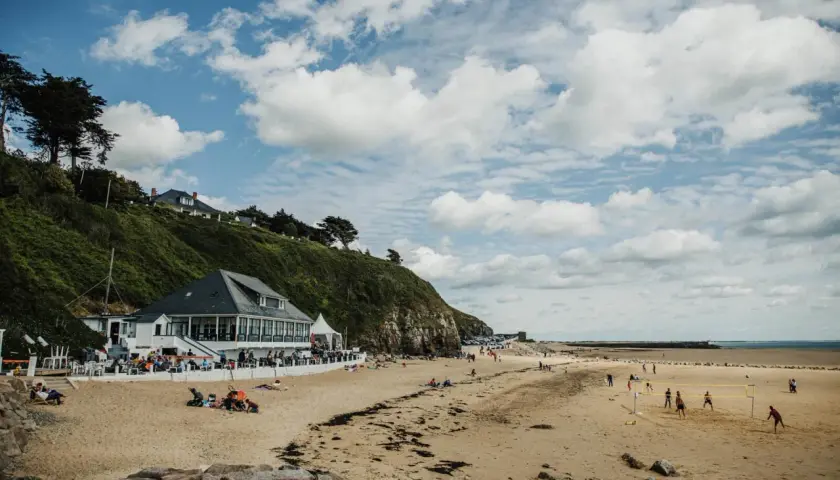 Plage normande avec restaurant en bord de mer, gens sur le sable et terrain de volley.