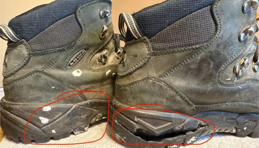 Two worn hiking boots with cracked and damaged soles, highlighted by red circles.