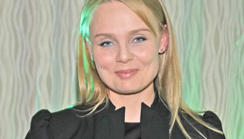 Patrycja Redo, z niebieskimi oczami i blond włosami, uśmiecha się. W tle falista zasłona.