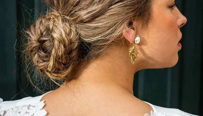 Elegante recogido pelo rizado boda invitada, con un moño trenzado y pendientes dorados.