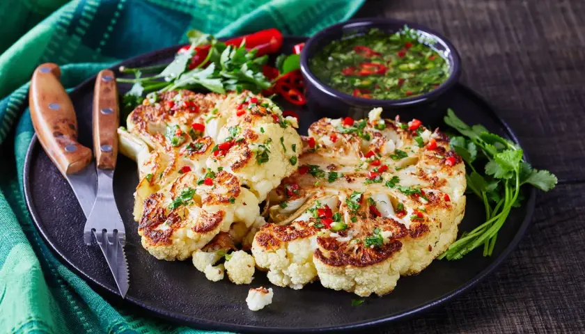 Idealny pomysł na kalafiora na obiad: pieczone steki z kalafiora z sosem chimichurri, posypane chili i pietruszką.