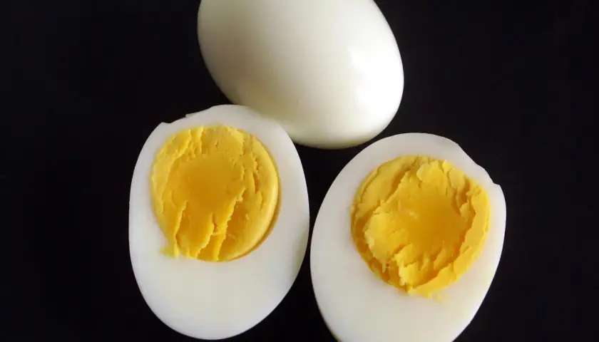 Un œuf entier et deux moitiés d'œufs durs sur fond noir, montrant le jaune bien cuit. Parfait pour une salade ou un en-cas.