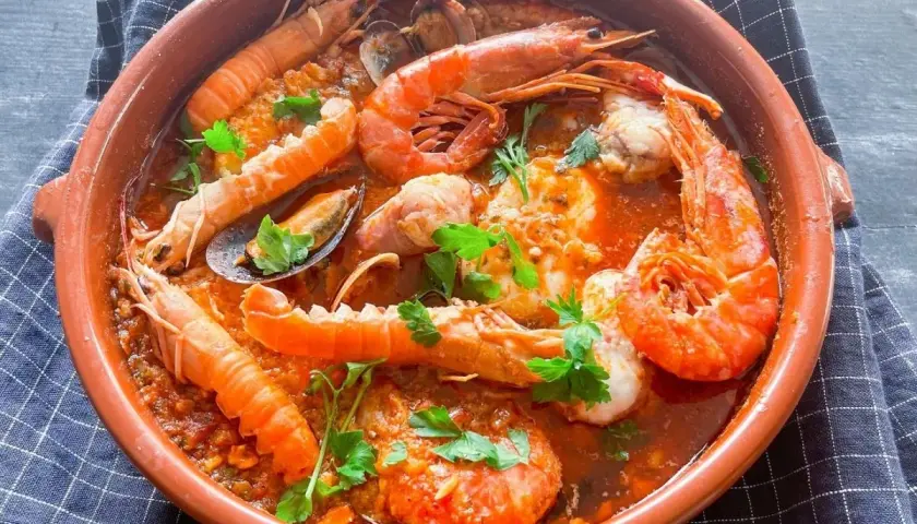 Deliciosa zarzuela de pescado con gambas, mejillones y cigalas en una cazuela de barro, decorada con perejil fresco.