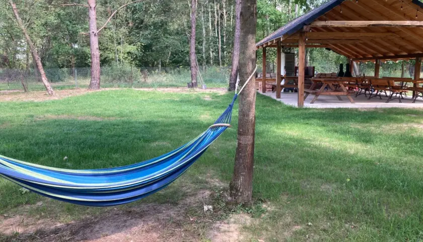 Kolorowy hamak w lesie, idealne miejsce na relaks podczas **camping Roztocze**. W tle drewniana wiata z ławami i stołami.