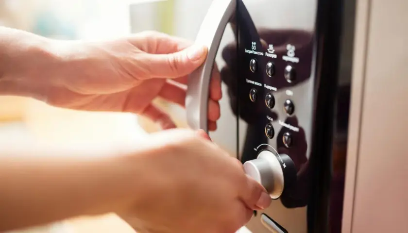 Mains de femme ouvrant un micro-ondes en inox. Elle tourne le bouton pour régler le temps de cuisson.