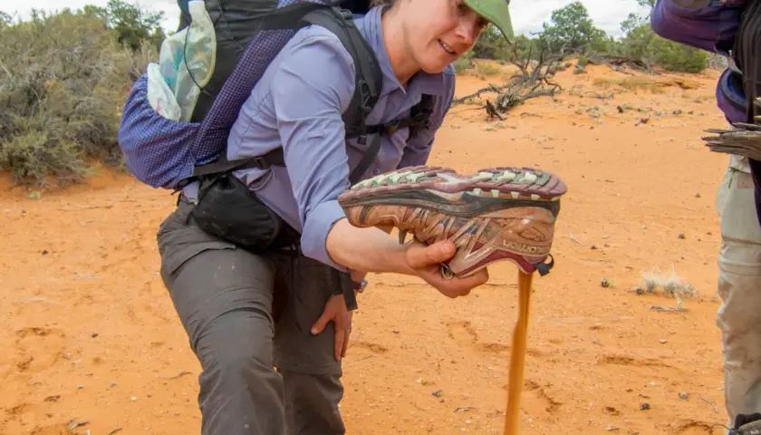 A hiker shakes sand from a shoe, demonstrating the challenge of finding the best shoes for hiking in sand.