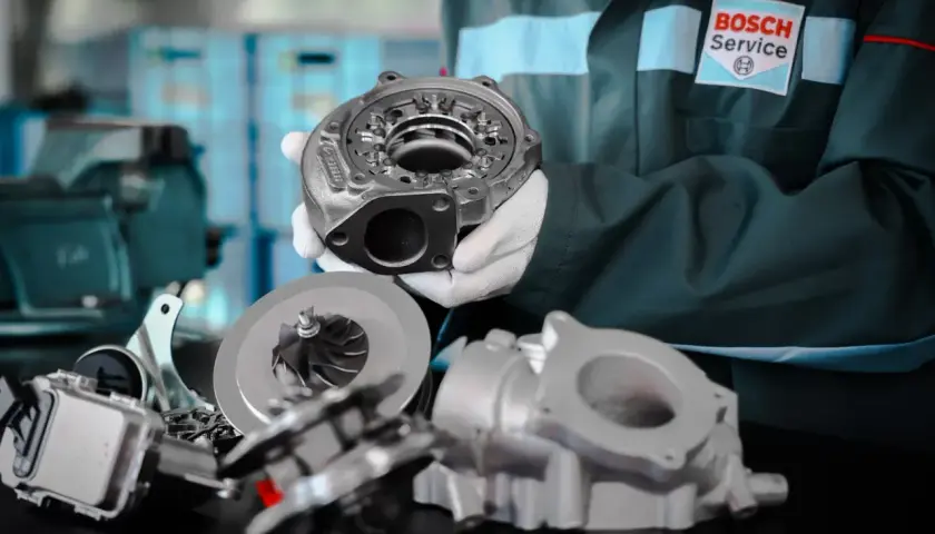 Mechanik w białych rękawiczkach prezentuje części turbosprężarki, pokazując jak sprawdzić turbinę w dieslu.
