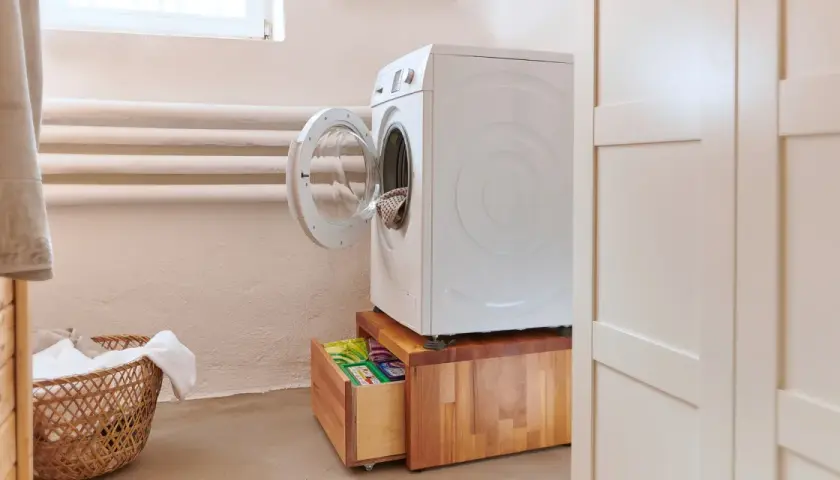 Waschmaschinen Podest selber bauen: Eine weiße Waschmaschine steht auf einem Holzpodest mit Schublade, darin Waschmittel.