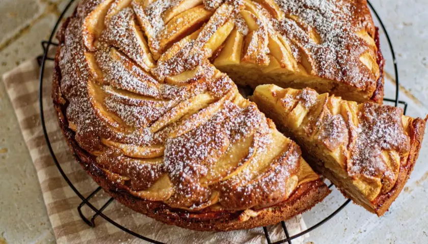 Gâteau mascarpone pommes, une tranche coupée, saupoudré de sucre glace. Un délice doré et moelleux.