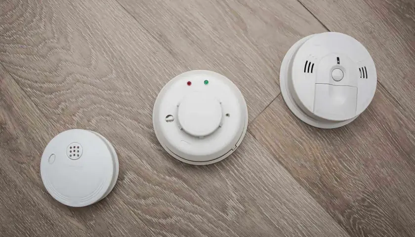 Trois détecteurs de fumée blancs sur un parquet. L'obligation d'installer un détecteur de fumée en entreprise est une mesure de sécurité essentielle.