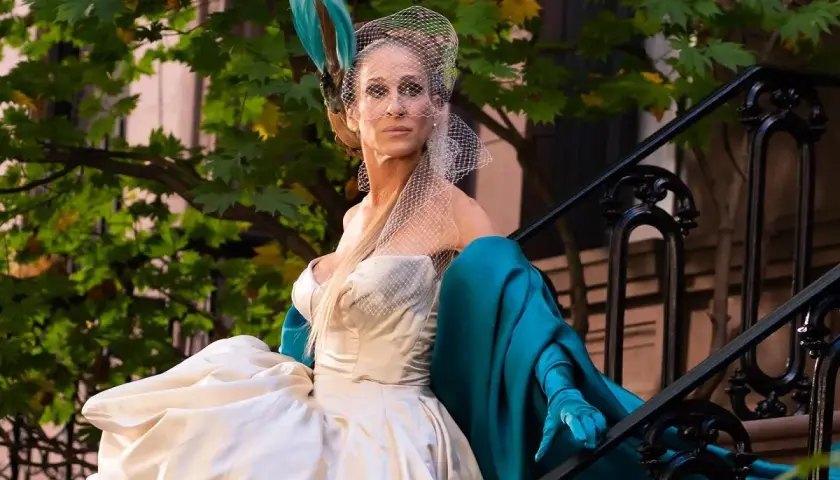 Carrie Bradshaw w białej sukni i turkusowym płaszczu, z welonem na głowie, siedzi na schodach. I tak po prostu.