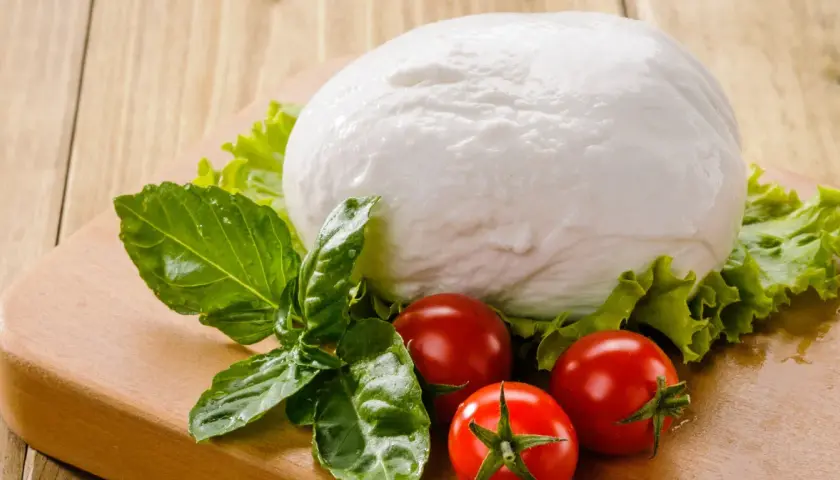 Kulista mozzarella, pomidorki i bazylia na desce. Czy mozzarella ma dużo białka? Tak, to świetne źródło białka!