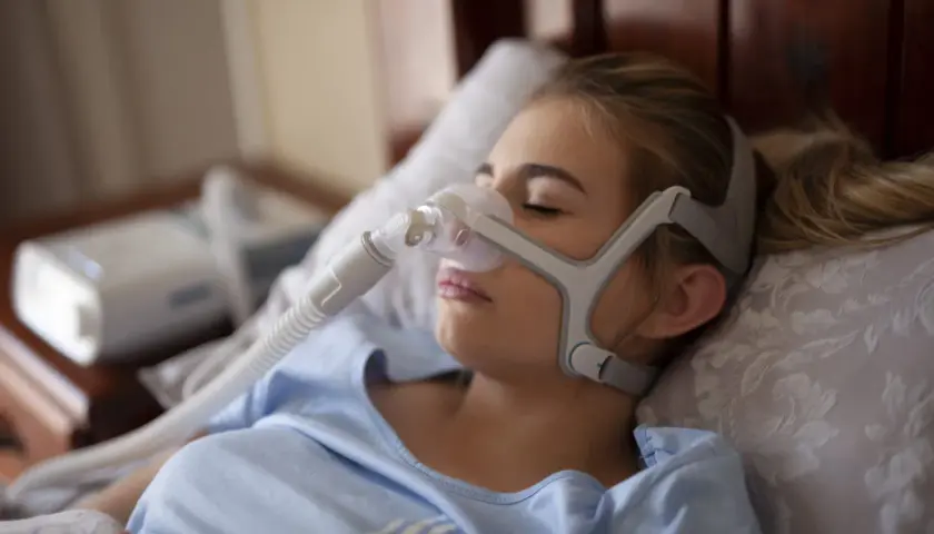 Kobieta śpi z maską CPAP, która pomaga na bezdech senny. Urządzenie zapewnia spokojny oddech przez całą noc.