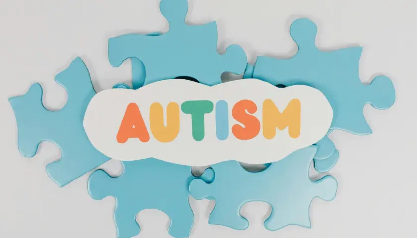 Niebieskie puzzle układanki otaczają chmurkę z napisem AUTYZM. Każdy element to unikalny fragment, jak w spektrum autyzmu i aspergerze.
