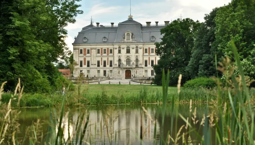 Zamek w Pszczynie, otoczony zielenią, z jeziorem w tle. Ciekawostki o jego historii i architekturze przyciągają turystów.
