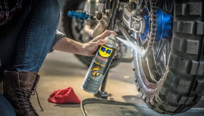 Persona en cuclillas engrasa cadena moto con spray WD-40.