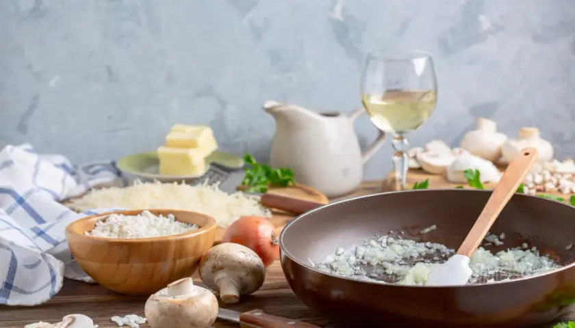 Préparation d'un risotto aux champignons, avec riz, oignons, champignons, parmesan, beurre et un verre de vin blanc.