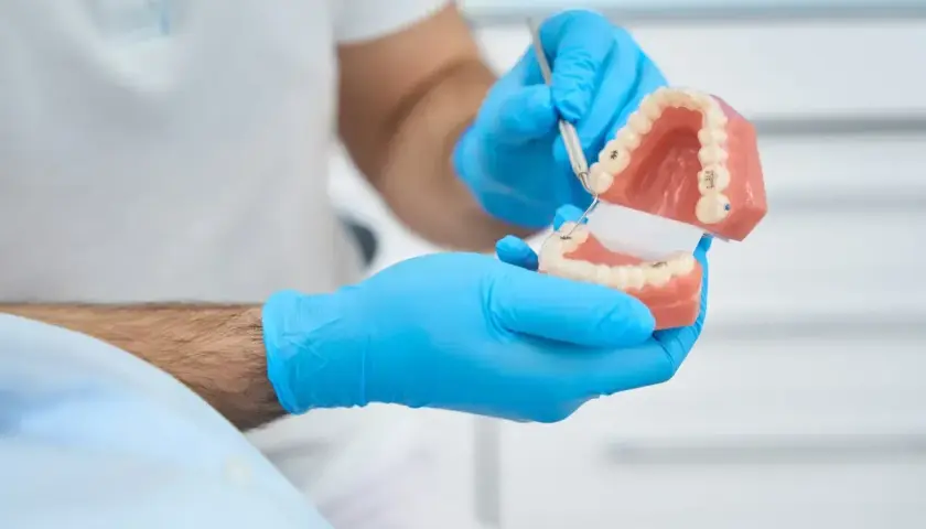 Dentysta w niebieskich rękawiczkach pokazuje model szczęki, wyjaśniając działanie protezy teleskopowej.
