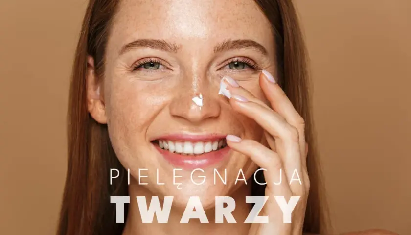 Uśmiechnięta kobieta z piegami nakłada krem na nos. To kluczowy element jej codziennego mycia twarzy i pielęgnacji.