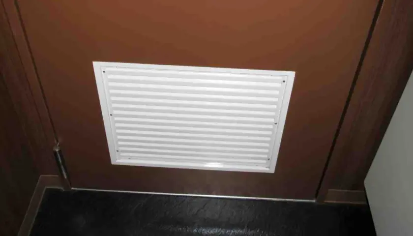Griglia di ventilazione bianca su porta marrone, ideale per capire come arieggiare una stanza senza finestre.