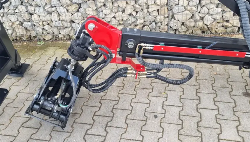Detailaufnahme eines roten und schwarzen Schwenkwerks für Forstkran mit Greifer und Hydraulikschläuchen.