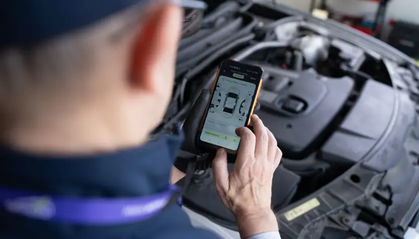 Mechanik sprawdza na telefonie raport z pomiaru lakieru i szczelin, szukając informacji o kodach błędów DTC.
