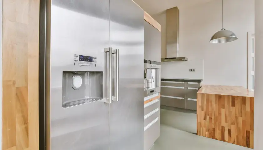 Nowoczesna kuchnia z lodówką w kolorze inox, drewnianą wyspą i stalowymi szafkami.