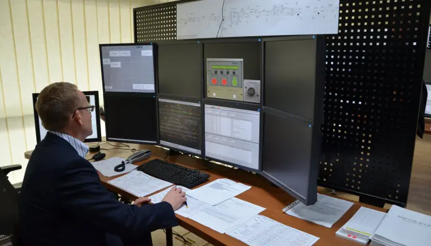 Dyżurny ruchu PKP analizuje dane na wielu monitorach. Na biurku dokumenty i klawiatura.