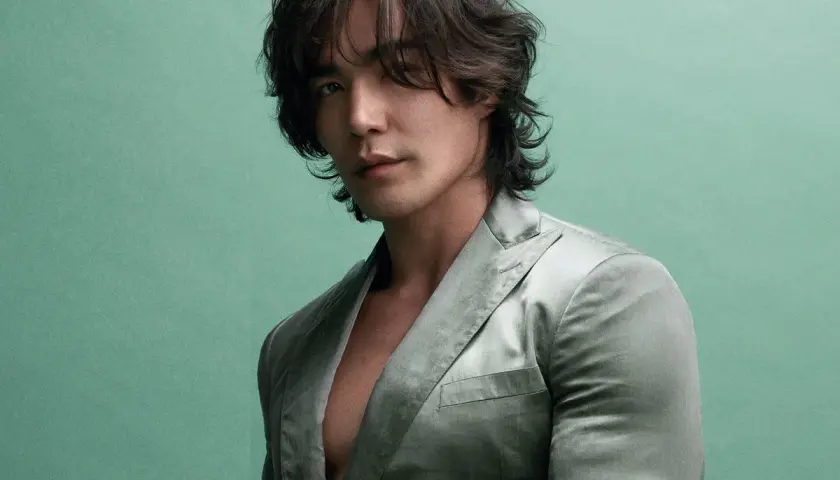 Ludi Lin, star de films et séries tv, pose dans un costume satiné sur fond vert menthe.