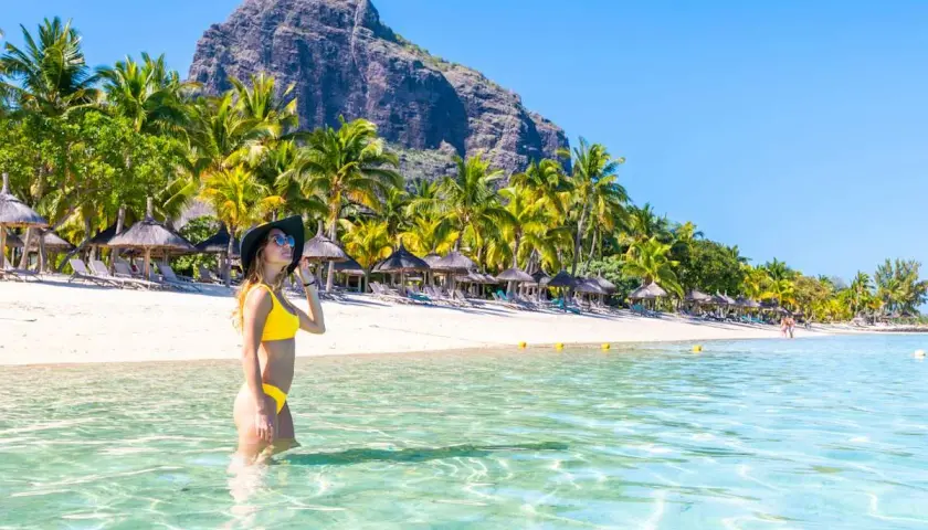 Frau im Bikini genießt das kristallklare Wasser an einem Traumstrand von Mauritius. Palmen und ein Berg im Hintergrund.