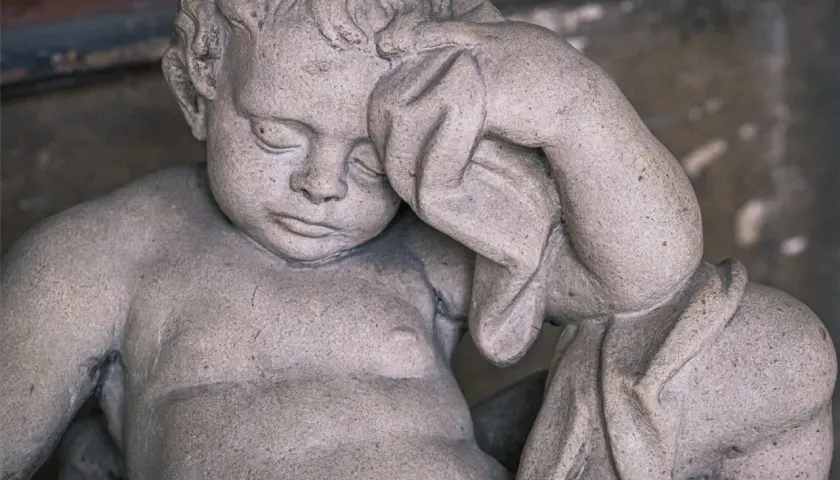 Kamienna rzeźba dziecka z zasłoniętymi oczami, jakby śniło o śmierci rodziców.