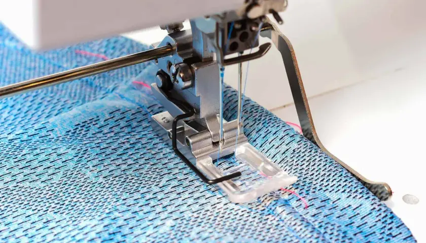 Sewing machine creating a coverstitch hem on blue patterned fabric.