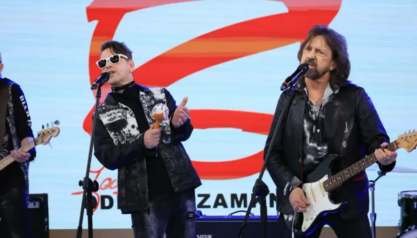 Zespół rockowy na scenie, wokalista w białych okularach i kolorowej kurtce, grający na marakasach. Obok gitarzysta w skórzanej kurtce. W tle logo "Jary Oddział Zamknięty".
