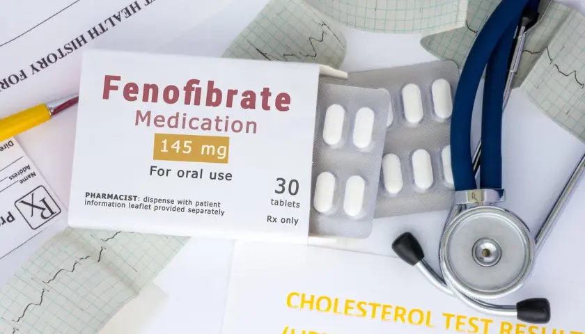 Opakowanie leku Fenofibrate 145 mg, tabletki, obok stetoskopu i wyników badań cholesterolu. Lipanthyl pomaga w leczeniu.