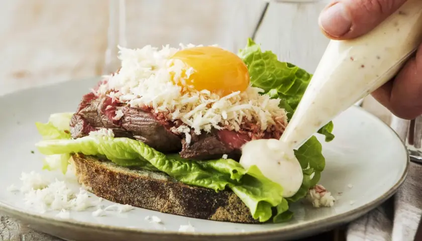 En lyxig smörgås med mört kött, äggula, sallad och riven ost. En klick krämig sås, kanske en carnitas cramby, spritsas på.