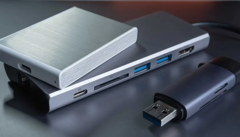 Ein silbernes Gehäuse für eine externe Festplatte liegt auf einem USB-Hub mit SD-Kartenleser und mehreren USB-Anschlüssen. Daneben ein USB-Stick.