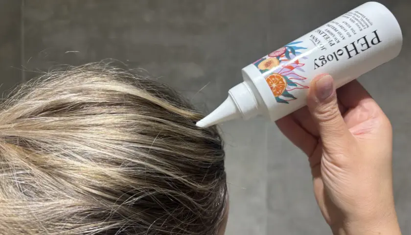 Aplikacja peelingu do skóry głowy z kwasami AHA na wilgotne włosy. Produkt w białej tubce z kolorowymi owocami.