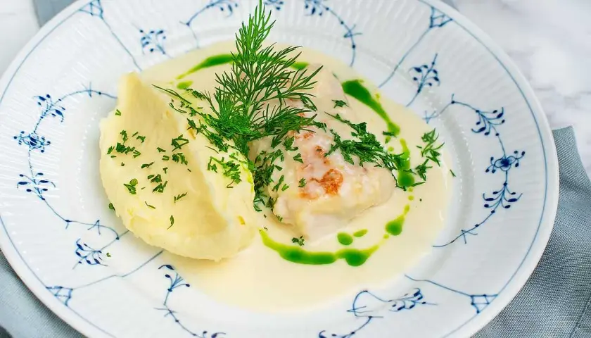 En vällagad torskrygg i ugn serveras med krämigt potatismos och en len sås, toppad med färsk dill och persilja.