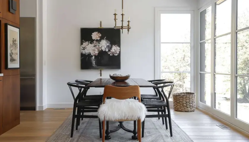 Modern dining room ideas: a dark wood table with black wishbone chairs, a floral painting, and a fluffy white accent chair.