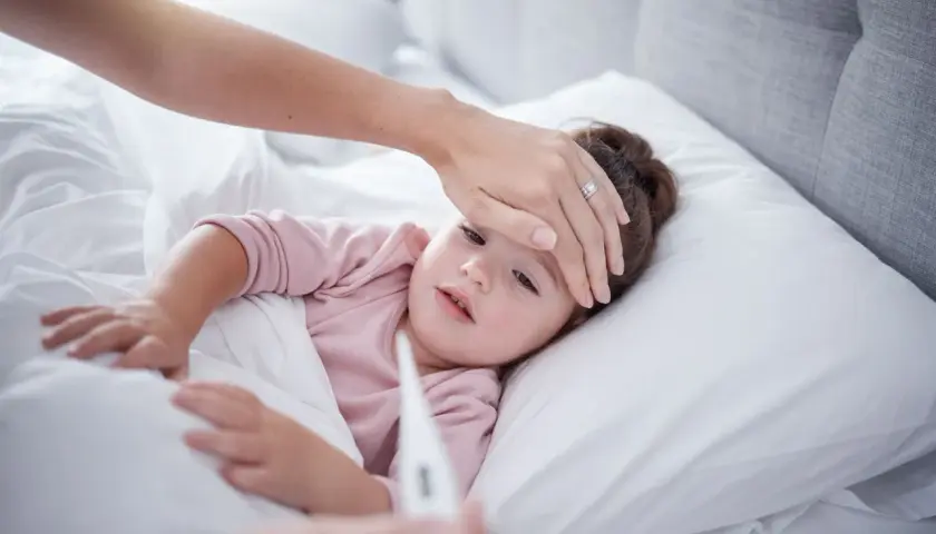 Madre revisa la fiebre de su hija. Si la fiebre persiste, considera el ibuprofeno para bebes.