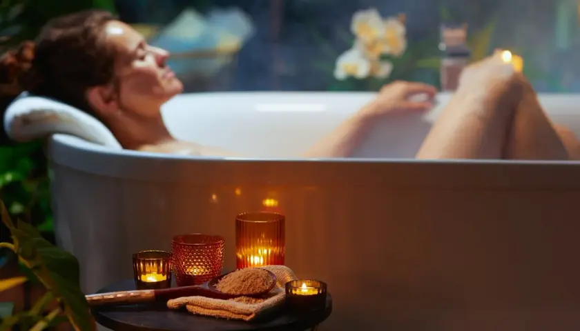 Kobieta relaksuje się w wannie, otoczona świecami i roślinnością. Czas na spokojne zabawy w wannie.