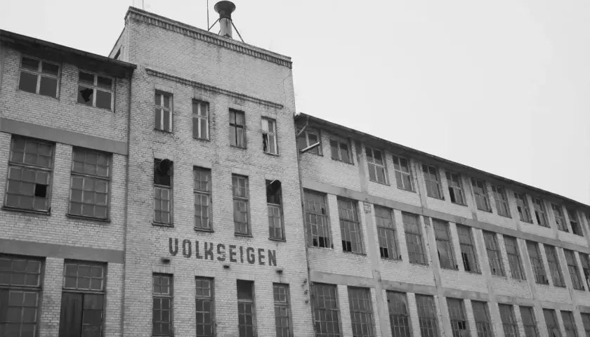 Verlassenes Fabrikgebäude mit der Aufschrift "VOLKSEIGEN", ein Zeugnis der Verstaatlichung in der DDR. Viele Fenster sind zerbrochen.