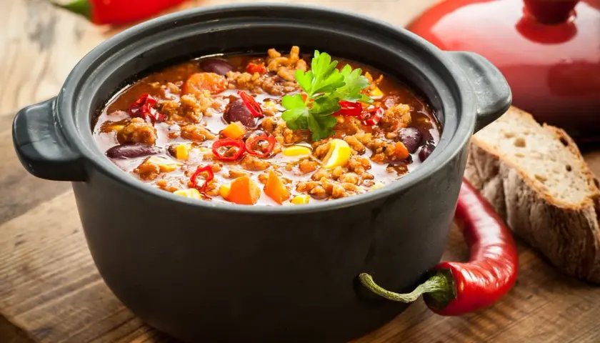 Un plat de chili mijoté dans une cocotte en fonte, parfait pour savoir si l'on peut mettre une cocotte en fonte au four. Accompagné de pain et de piments.