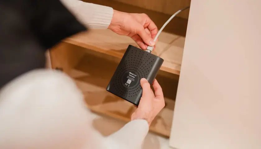Man conectando un cable a un **home gateway** negro dentro de un mueble de madera.