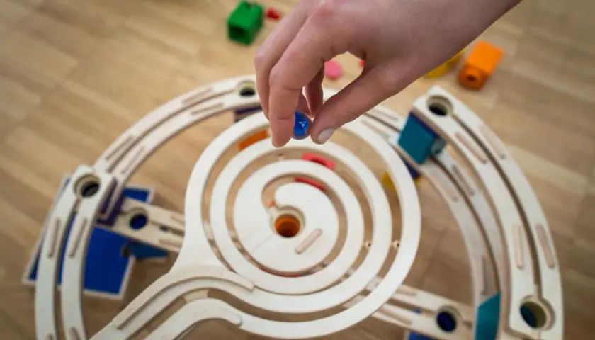 Mano che rilascia una biglia blu su una pista a spirale in legno, parte di giochi con le biglie.